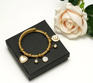 Détail du bracelet câble doré avec breloques cœur, lune et cristal sur boîte à bijoux