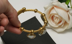 Détail de bracelet torsadé doré avec breloque cœur en nacre et zircons brillants