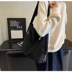 Detail of black canvas tote bag showing silver zipper pocket and wide shoulder strap