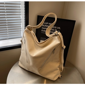 Close-up of beige canvas bag with multiple zipper pockets and metallic silver hardware details