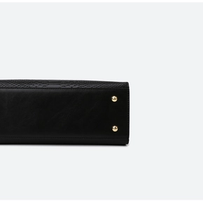 Detailed close-up of black leather bag base featuring snakeskin texture and gold metal feet
