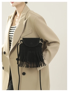 Détail d'un sac bandoulière en daim noir à franges porté sur un blazer beige chic