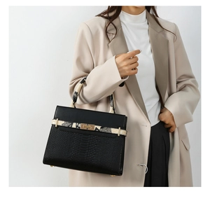 Model holding a black crocodile-embossed leather tote bag with snakeskin trim and gold lock