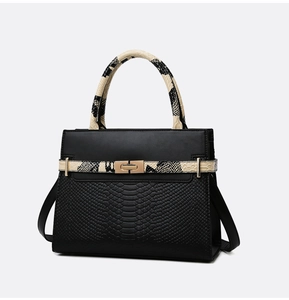 Detail of black textured leather bag with beige snakeskin handles and gold rotary lock