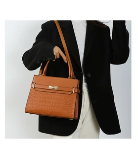 Close-up of caramel leather tote bag with crocodile texture and golden metal twist lock