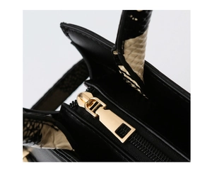 Detail of black faux leather bag featuring golden zipper and exotic reptile texture handle