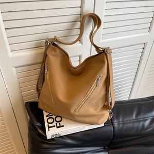 Large khaki canvas hobo bag with zip details on a sofa, minimalist casual style