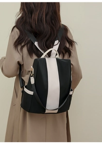 Detail of a black and cream contrast backpack with golden hardware worn on a beige coat