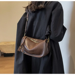 Detail of dark brown saddle bag featuring smooth synthetic leather and side tassel accent
