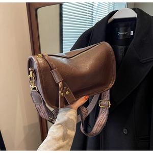 Close-up of brown faux leather saddle bag with geometric patterned wide strap and gold hardware