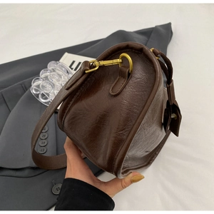 Detail of dark brown saddle bag with vintage oil-wax texture and antique gold hardware