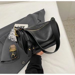 Detail of black textured faux leather saddle bag with gold zipper and dual shoulder straps