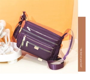 Detailed view of the dark purple nylon crossbody bag with multiple gold zippers