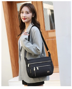Detailed view of black nylon shoulder bag with multiple gold zippers and compartments