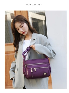 Close-up of a purple multi-zipper nylon crossbody bag with adjustable shoulder strap