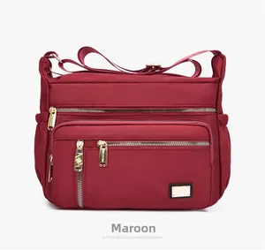 Detail view of burgundy nylon crossbody bag featuring multiple functional zipper pockets
