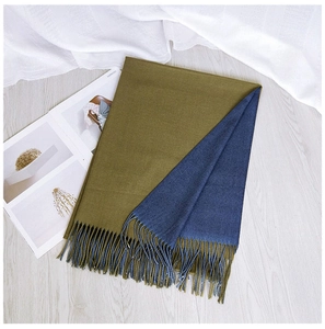 Detail of double-sided olive green and navy scarf with fringes on light wood floor