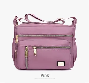 Close-up of pink Oxford fabric crossbody bag with multi-layer gold zippers and wide strap