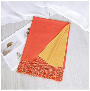 Flat lay detail of a two-tone orange and yellow scarf with fringed edges on wood