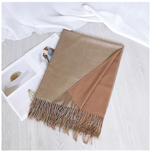 Close-up of a two-tone warm scarf with delicate tassels on a minimalist wooden background