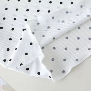 Close-up of white polka dot fabric with ribbed texture and clean hemline stitching