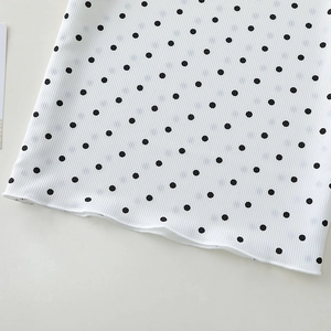 Detailed macro view of white ribbed knit fabric with black polka dots and hemmed edges
