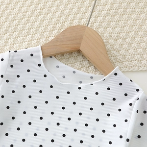 Detail of white polka dot baby pajamas featuring ribbed texture and scalloped collar design