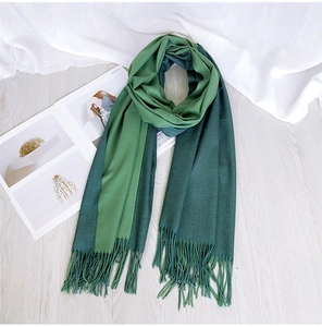 Detail of a two-tone green knit scarf with elegant fringe trim on a wooden floor