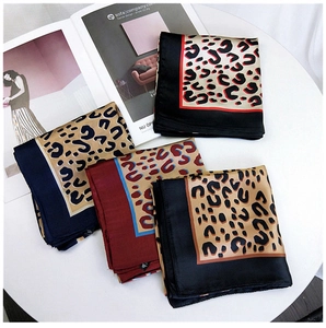 Flat lay of four leopard print satin scarves in various colors on a white table display