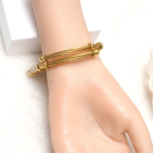 Detail of gold cable twist bangle featuring a sparkling pave set round charm on wrist