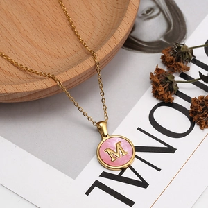 Close-up of golden stainless steel necklace with pink shell M-letter pendant on a magazine