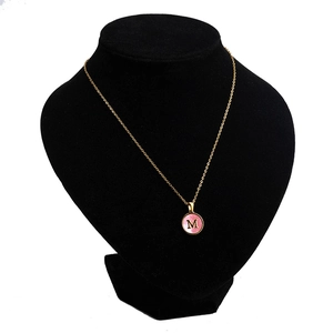 Macro detail of gold-plated pendant featuring pink shell inlay and letter M on a necklace