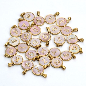 Macro detail of 18K gold plated stainless steel pendants with pink shell alphabet charms