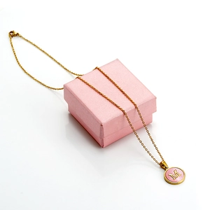 Close-up of 18K gold stainless steel M-letter necklace on a pink textured jewelry box