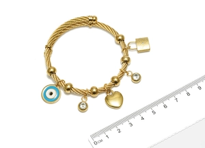 Detail eines goldenen Kabel-Armreifs mit Evil Eye, Herzanhängern und Maßstab