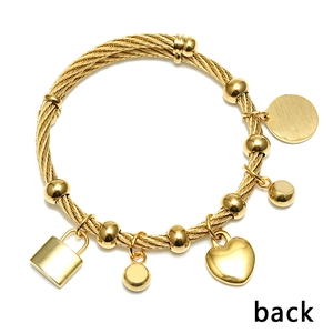 Detail eines goldenen gedrehten Armreifs mit Herz- und Schlossanhängern und Perlen