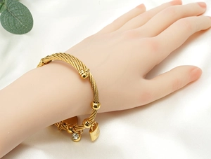 Detail eines gedrehten Goldarmbands mit Zirkonia-Kugel und Stern-Schloss-Anhängern