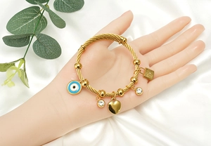 Detail eines goldenen Kabelarmbands mit Evil Eye-, Herz- und Schloss-Anhängern