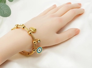 Detail eines Goldkabel-Armbands mit Herzanhänger, Kristall und blauem Evil Eye Anhänger