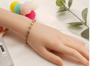Detail eines goldenen Evil-Eye-Armbands mit bunten Anhängern auf weißem Seidenhintergrund