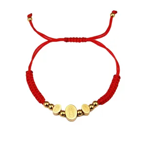 Detail of red braided rope bracelet featuring gold religious pendants and adjustable cord