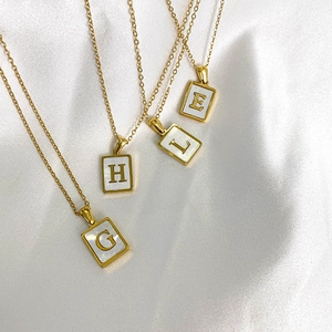 Détail de pendentifs alphabétiques carrés dorés avec nacre sur soie blanche