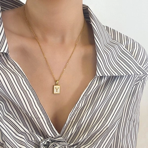 Détail du pendentif carré en nacre avec lettre Y dorée sur une fine chaîne dorée