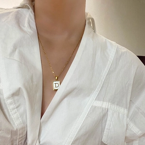 Détail d'un collier carré doré avec nacre et lettre D porté sur une chemise blanche
