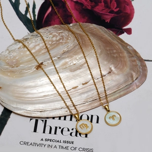 Detalle de collares de zodiaco bañados en oro de 18K con nácar blanco sobre una concha marina