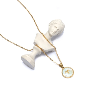 Collar Aries dorado con colgante de nácar blanco sobre una escultura artística