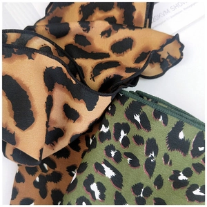 Detailed view of leopard print silk scarves in brown and green with rolled edges