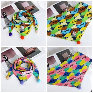 Detail of kids triangle scarf featuring floral patterns, colorful pom-poms, and a bear patch