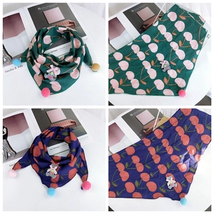 Close-up of knit triangle scarf with cherry patterns, bear patch, and colorful pom-poms