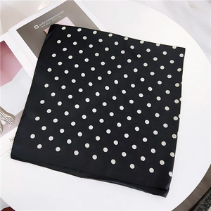 Classic black square silk scarf with white polka dots on a minimalist modern white table